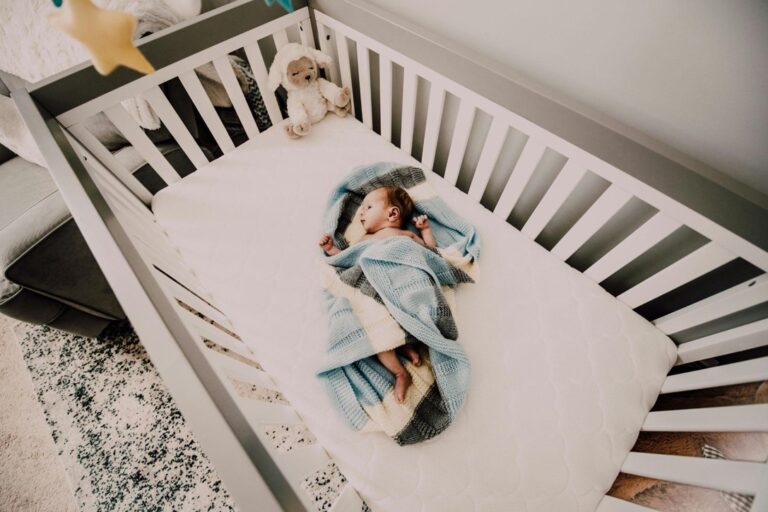 A Baby is lying in a crib, top view, light-grey tones.